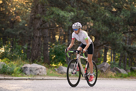 青年女赛车手骑着路自行车在夏日热火的森林中走免费道路 健康生活方式概念公园街道森林女孩晴天头盔成人城市运动女性图片