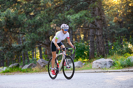 青年女赛车手骑着路自行车在夏日热火的森林中走免费道路 健康生活方式概念公园城市晴天爱好成人自由活动头盔森林女孩图片