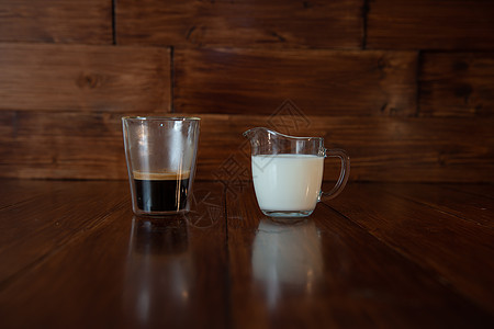 在玻璃的牛奶罐中 装着一杯咖啡 在明亮的玻璃杯里杯子用具工作室奶牛水壶营养桌子木头奶油反射图片