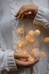 手掌上的光 女手拿着一个带柳条圆球的花环 身穿白色毛衣 手里拿着圣诞灯的女孩 温暖的新年气氛 柔和的焦点背景风格魔法装饰辉光女性图片