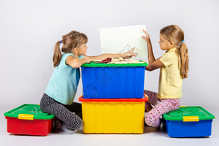 塑料闺蜜团两个女孩坐在大玩具箱上 看玩具装配指示 女背景