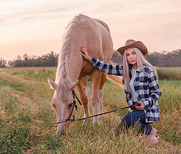 穿着牛仔帽和蓝牛仔裤的年轻金发女孩青少年蓝色村庄动物场地草地植物衬衫金发女郎农场图片