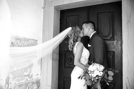 亲吻 新娘和新郎在教堂门前温柔地亲吻裙子男性婚姻花束新婚夫妇家庭套装门户网站奢华图片