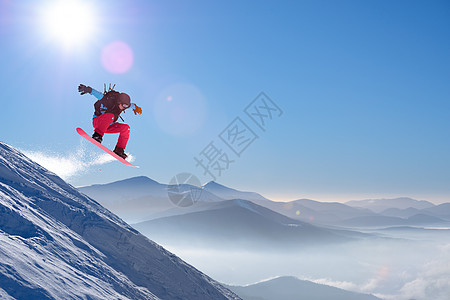 滑雪运动员在太阳尼日跳上山中红雪板 滑雪和冬季运动粉末蓝色空气单板假期木板头盔行动旅行下坡图片