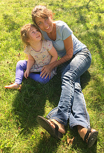 年幼母亲和学龄前儿童在阳光下的青草上微笑图片