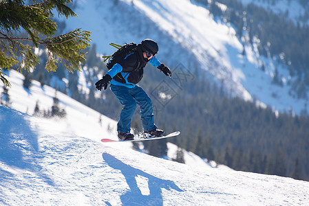 滑雪运动员在太阳尼日跳上山中红雪板 滑雪和冬季运动乐趣头盔速度假期滑雪板空气下坡天空木板单板图片