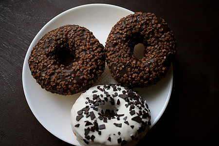 三个甜甜圈在白色盘子上 棕色背景巧克力美食纹理圆圈杏仁糕点奶油面包糖果早餐图片
