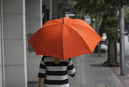 背对着女人的眼神 带着橙色雨伞在街上行走雨衣胡同天气女性快乐季节微笑公园城市乐趣图片