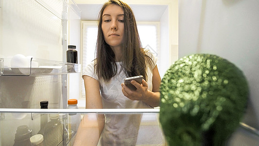 妇女在冰箱里用智能手机制作食物清单图片