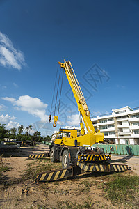 有上升的伸缩臂的黄色汽车起重机在户外 建筑工地上的移动式建筑起重机 起重机在施工大楼下等待工作 重工业机器繁荣蓝色容量三角帆活动图片