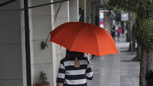 背对着女人的眼神 带着橙色雨伞在街上行走快乐季节下雨女性外套沉思公园成人微笑天气图片