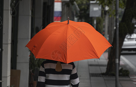 背对着女人的眼神 带着橙色雨伞在街上行走女性微笑沉思胡同城市街道雨衣女士快乐乐趣图片