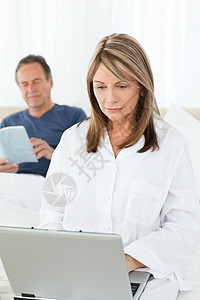 女人看她的笔记本电脑 而她丈夫正在阅读工作家庭键盘乐趣喜悦互联网老年女性女孩闲暇图片