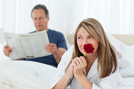快乐的女子在她丈夫看报纸时闻着她的玫瑰香味女士已婚幸福展示生日夫妻拥抱礼物投标阅读图片