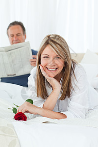 幸福的女人带着玫瑰 而她的丈夫正在看报纸沙发拥抱展示阅读女士男人香味客厅投标夫妻图片