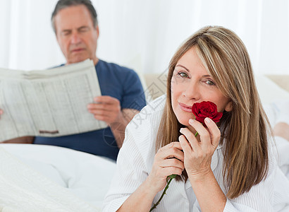 快乐的女子在她丈夫看报纸时闻着她的玫瑰香味微笑夫妻礼物生日阅读展示房子投标幸福男人图片