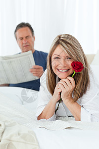 幸福的女人带着玫瑰 而她的丈夫正在看报纸惊喜拥抱房子生日投标沙发微笑香味已婚展示图片