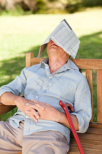 高级男子睡在长凳上报纸绿色植物公园退休男人帽子男性长椅幸福闲暇图片