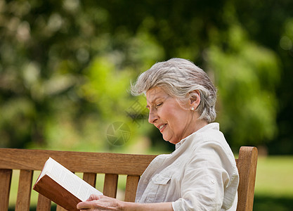 退休妇女在法官席上看书小猪女性农村微笑女士笑声相机肩膀公园座位图片