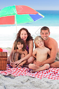 家人在沙滩上 在孤单的雨伞下野餐图片