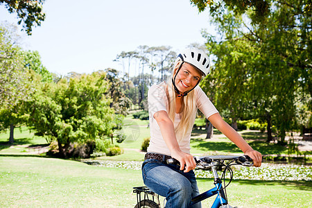 在公园里的女人 骑着自行车乐趣运动锻炼幸福相机微笑女士绿色女性享受图片