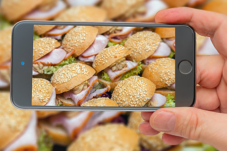 盘子上的冷开胃菜 多排的汉堡包加培根和草药 智能手机屏幕上的三明治图片