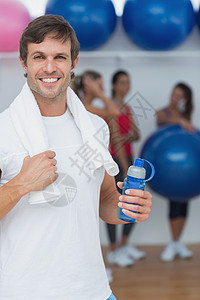 男子在健身工作室拿着水瓶 有朋友背景的人护理健身房运动服男人瑜伽健身室活动俱乐部运动毛巾图片