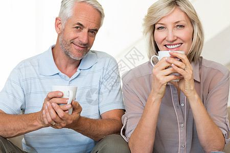 微笑的成年夫妇与咖啡杯坐在沙发上杯子咖啡饮料长椅夫妻家庭生活男性男人房子客厅图片