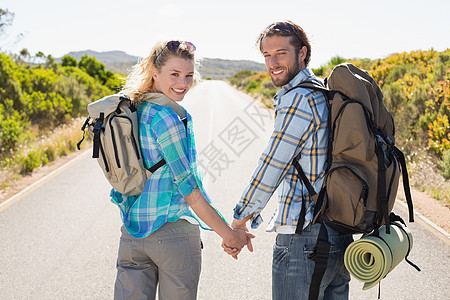 坐在路上的一对迷人的情侣手握着镜头微笑便车太阳镜农村女性勘探环境浅色金发女郎冒险家登山图片