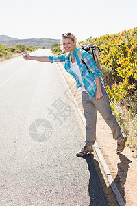 乡村公路上迷人的金发金色搭车徒步旅行远足女性晴天浅色微笑冒险便车活动头发快乐图片