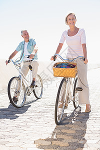 快乐的老年情侣去骑自行车退休微笑棉布裤夫妻阳光闲暇女士休闲衬衫篮子图片