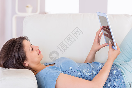 在沙发上用她平板电脑的 漂亮褐色头发药片住所休假触摸屏长椅说谎休闲女士家庭生活空闲图片