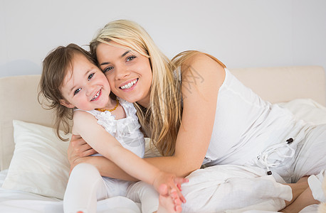 快乐的母亲和女儿坐在床上的肖像图片