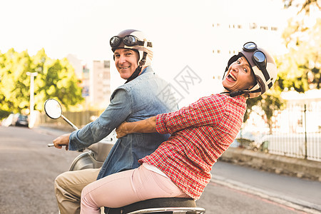 快乐的成熟情侣在城里骑摩托车活动方式晴天拥抱车辆浅色驾驶都市男性城市生活图片