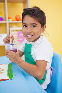 在教室的桌子上画可爱的小男孩教育童年班级课堂男性幼儿园创造力围裙男生微笑图片