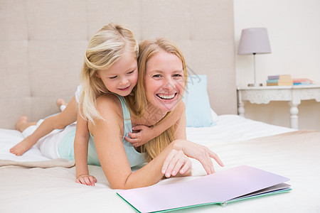 可爱的小女孩和妈妈在床上看书浅色快乐母亲家庭住所公寓阅读棉被头发闲暇图片
