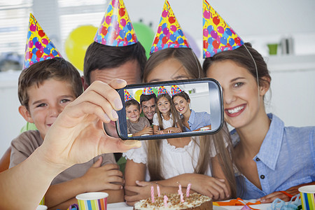 手持智能手机显示的复合图象女性派对乐趣住所母亲气球男生桌子孩子杯子图片
