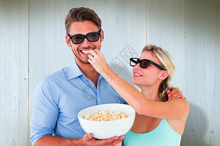 喜悦的年轻情侣身戴3D眼镜吃爆米花的综合画面计算机夫妻快乐女朋友木头男朋友男性女性蓝色粮食图片