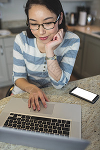 年轻妇女在厨房用笔记本电脑快乐住所台面工作女性技术微笑家庭沟通在家图片