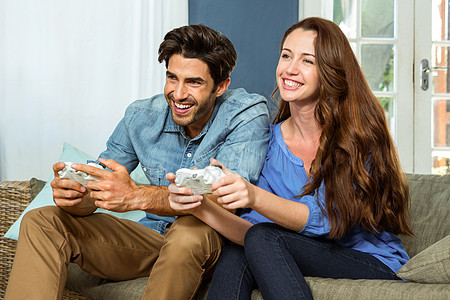 年轻夫妇坐在沙发上玩电子游戏公寓游戏休闲活动幸福服装俏皮女性乐趣微笑图片