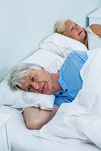 深思熟虑的老年男子在床上放松 而女人打呼噜图片
