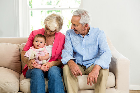 快乐的祖父母坐在沙发上看着婴儿图片