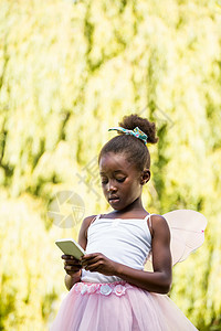 穿着童话服装并使用智能手机的可爱混合种族女孩幸福女性乐趣专注黑色绿色公园童年电话屏幕图片