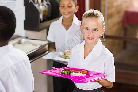 在学校食堂里拿着餐盘的微笑女学生图片