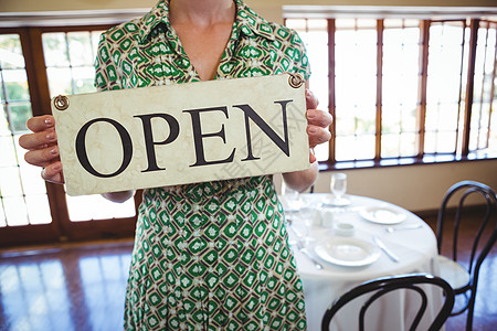 女人拿着一个有开放标志的牌子零售咖啡店盘子服务器营业时间女士窗户酒吧饮料酒店图片