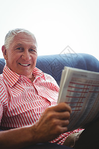 年长男子坐在沙发上 一边拿着报纸看着照相机看电视图片