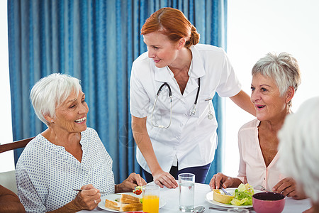 护士在早餐时微笑 看着老人长者老年退休庇护所享受诊所橙汁托儿所白色剥离住宅图片