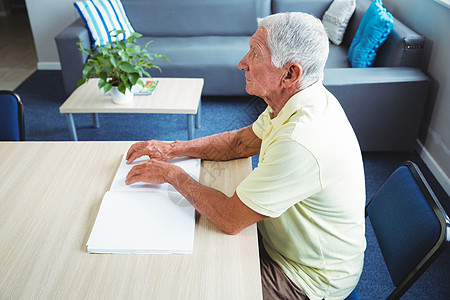 高年男子使用盲文阅读老年人老年托儿所桌子住宅病人医疗保险退休保健医学图片
