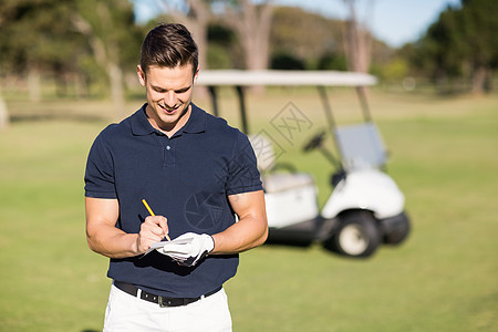 微笑高尔夫球手在记分卡上写作图片