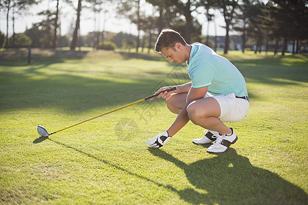 男人运动年轻人把高尔夫球放在Tee的侧面视图背景